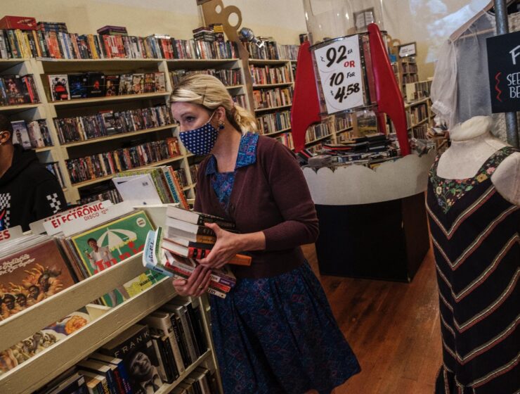 A photo of a woman working in a small retail store wearing a mask.