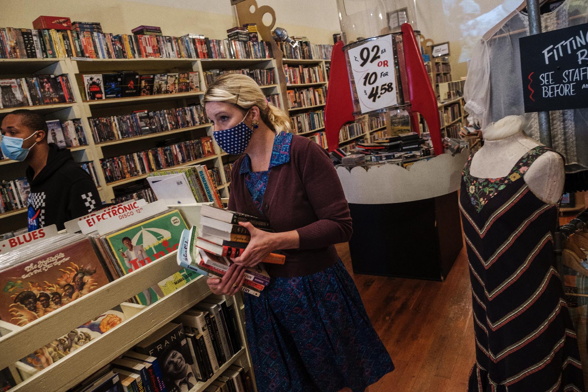 A photo of a woman working in a small retail store wearing a mask.