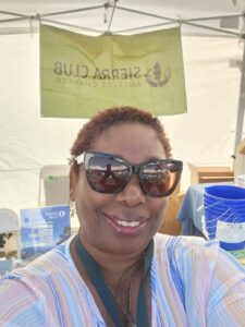A photograph of a woman smiling in front of a Sierra Club flag.